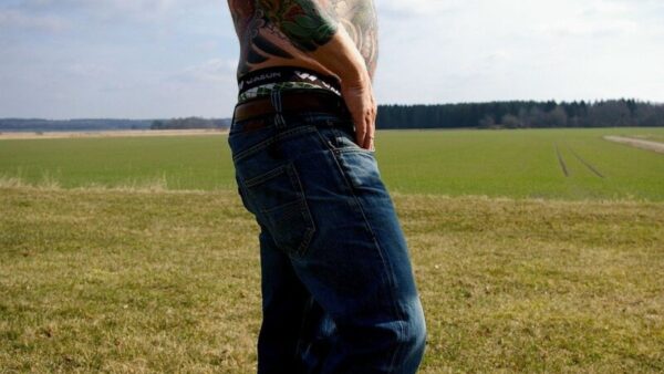 man with upper body tattoos in blue jeans